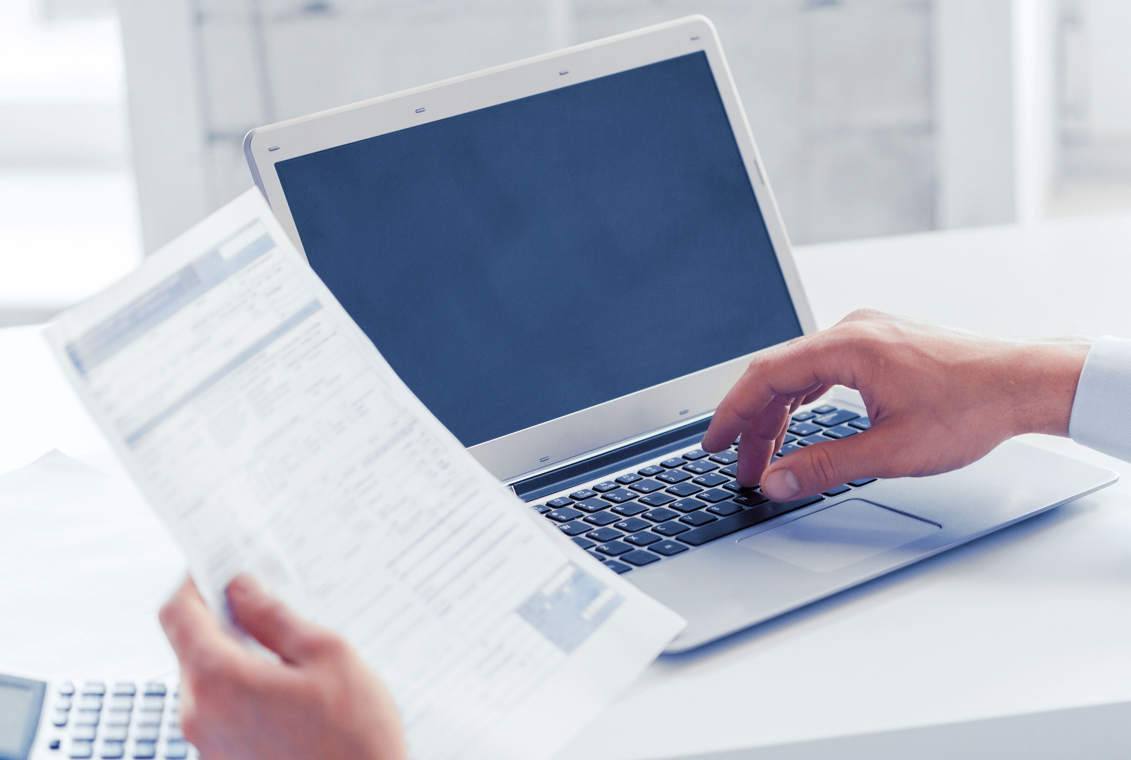 This photograph depicts a close-up of a person's hands typing on a silver laptop. 