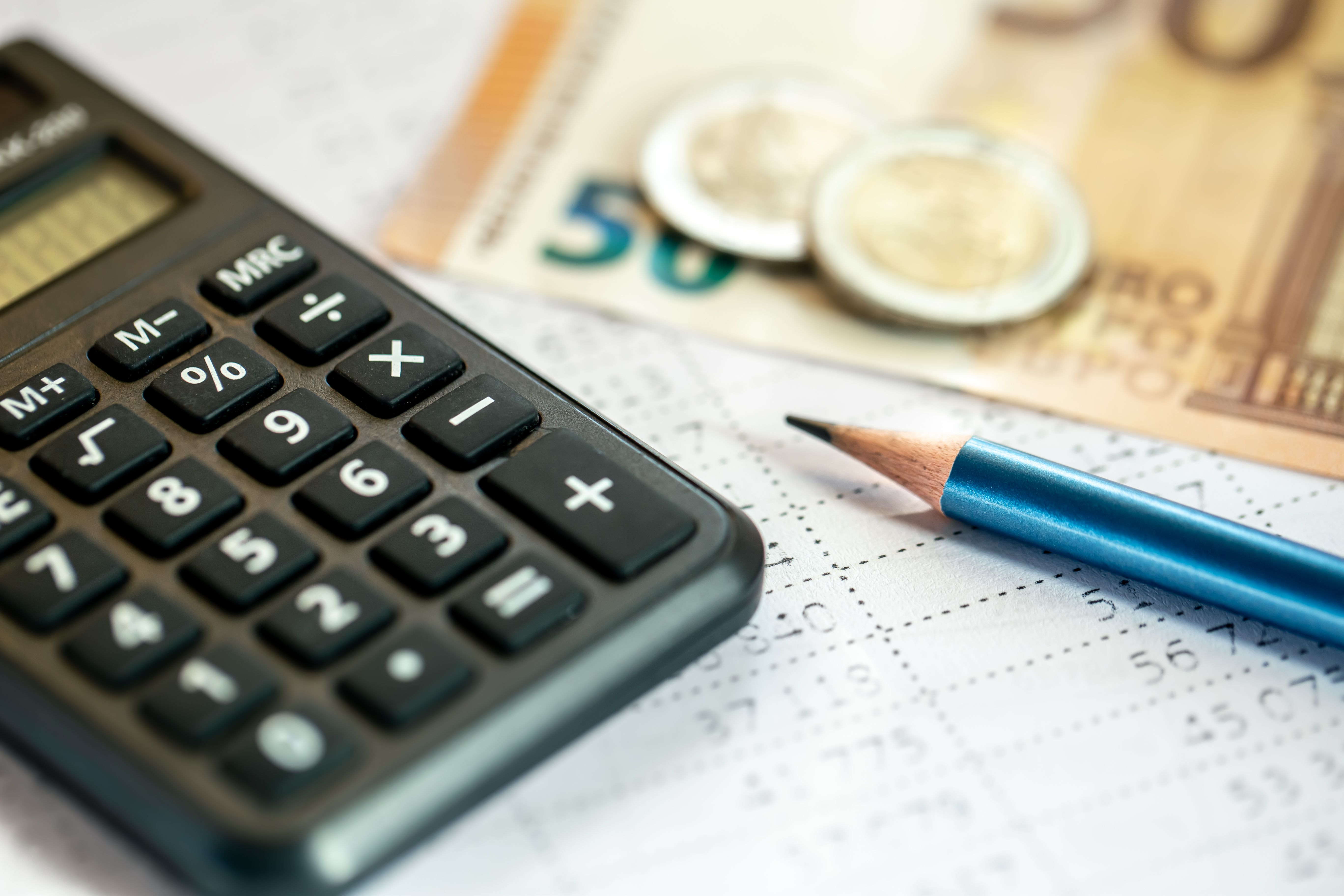 A photograph featuring a black scientific calculator with white numerals, a blue pencil with a sharp point, and a stack of Euro banknotes, including a 50 Euro note, on a white grid paper.