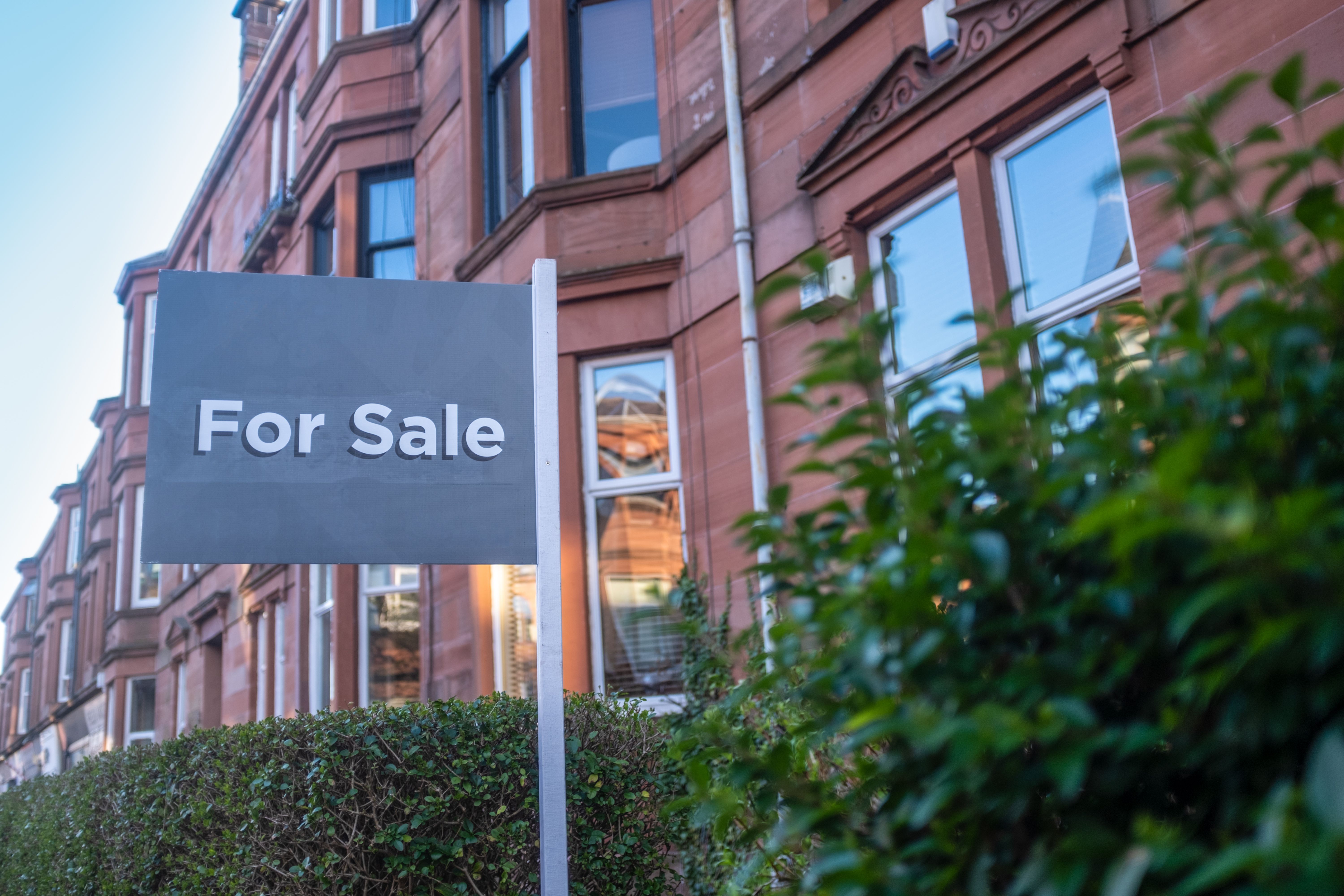 Photograph of a "For Sale" sign in front of a row of red-brick Victorian townhouses with tall, narrow windows