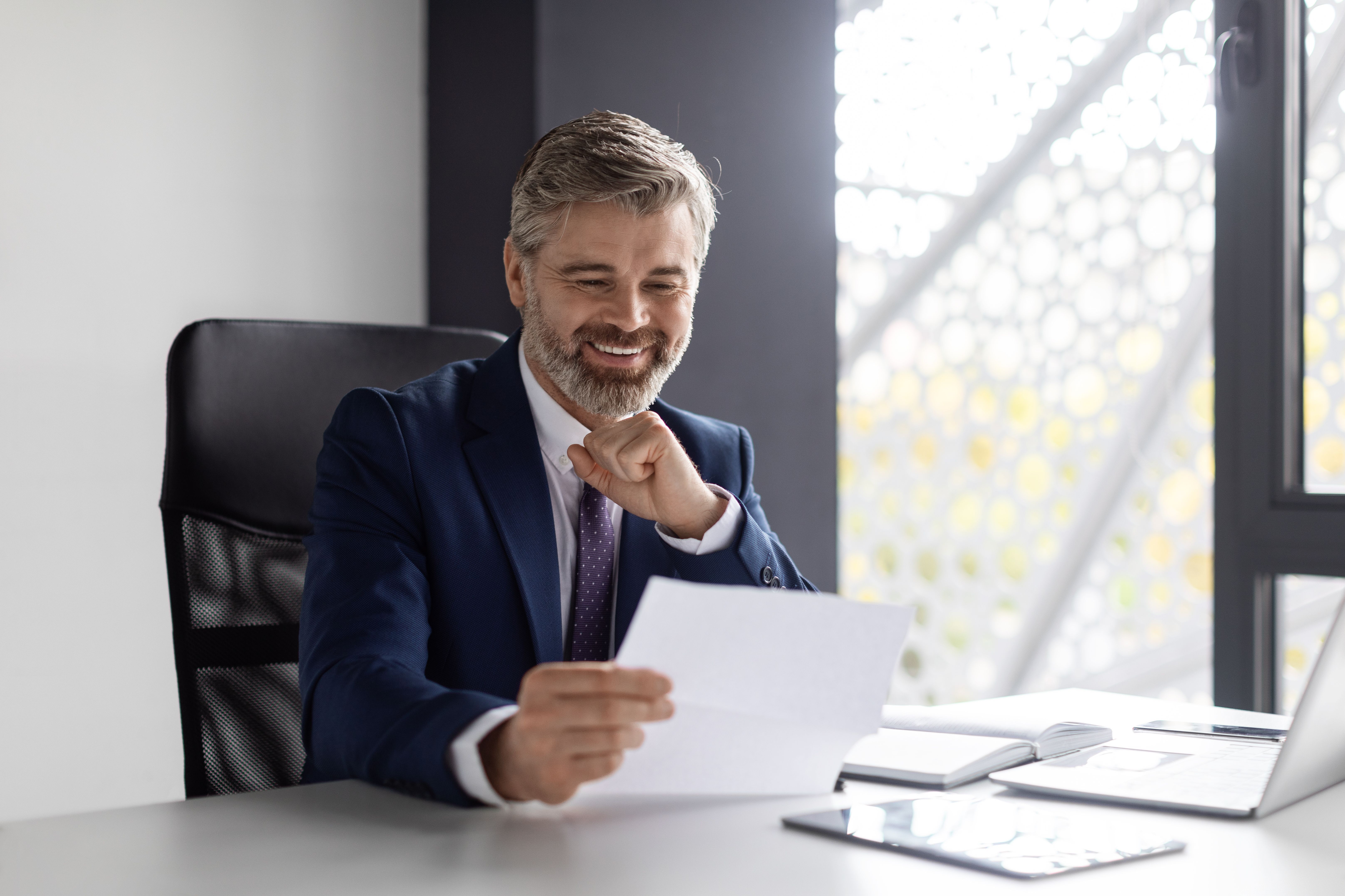 Photograph of a middle-aged white man with short, salt-and-pepper hair, sitting at a modern office desk.