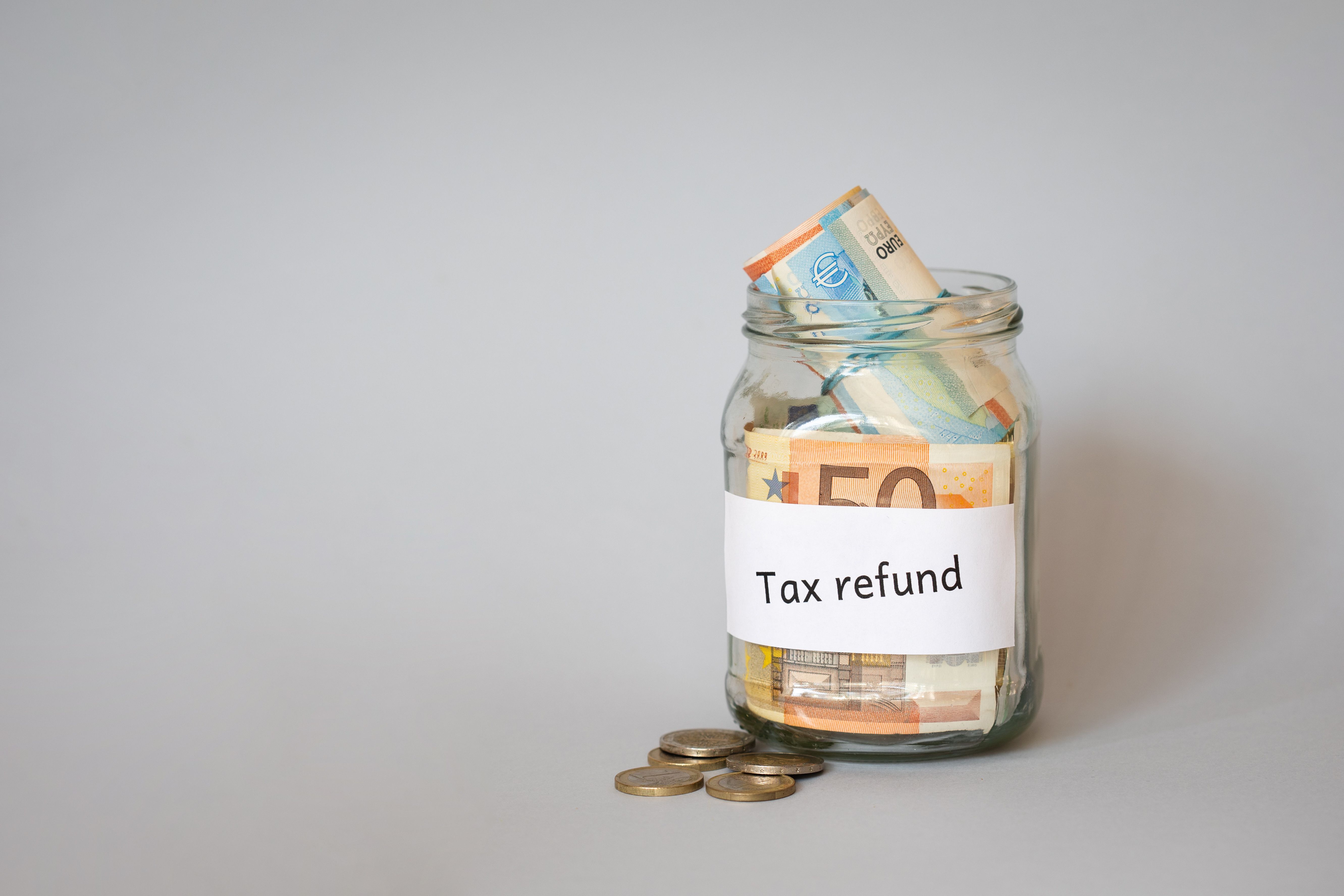 A photograph depicts a clear glass jar filled with various denominations of Euro currency, including 10, 20, and 50 Euro notes.