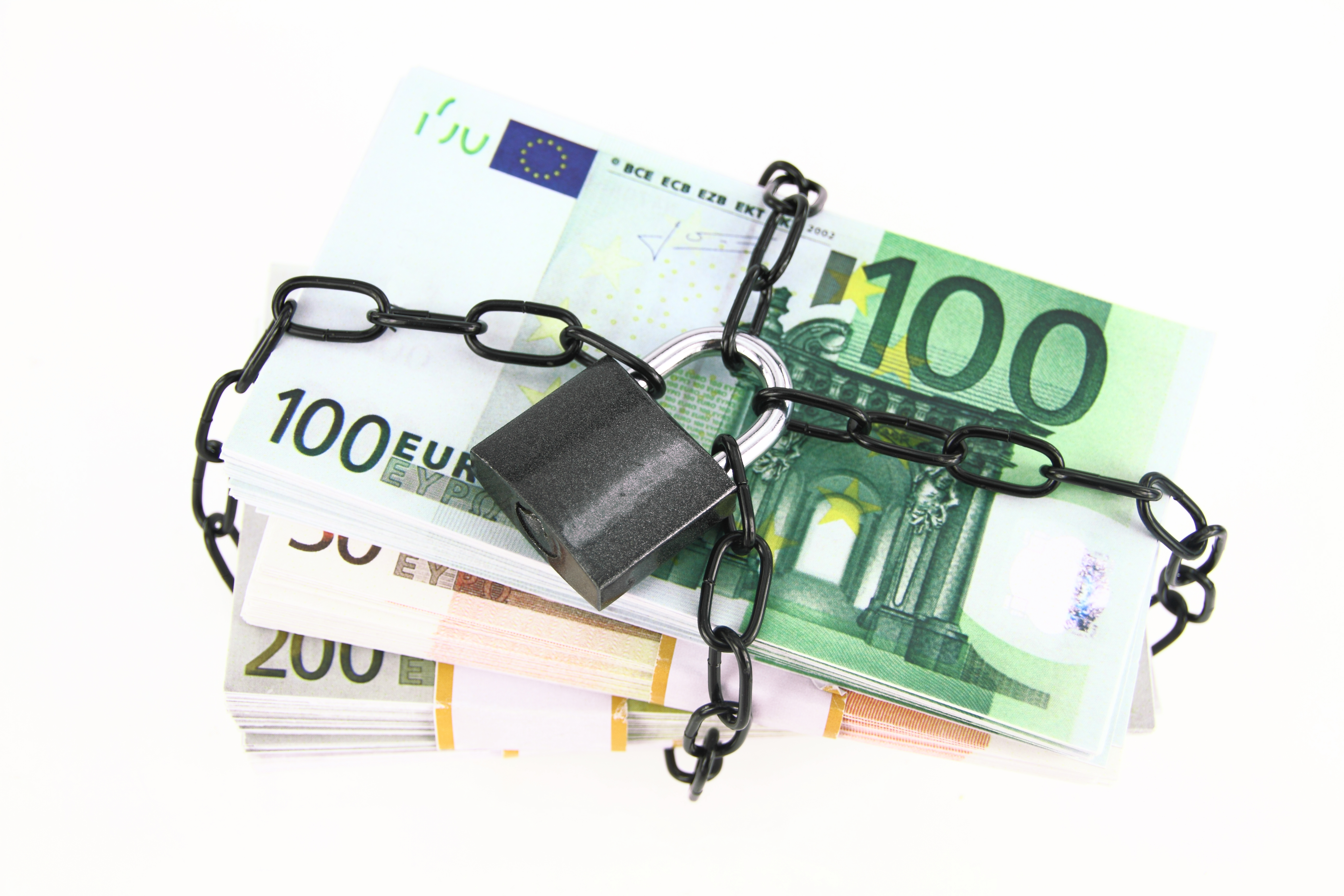 This photograph depicts a pile of 100-euro banknotes bound together with a thick black chain, symbolizing financial constraints or security measures.