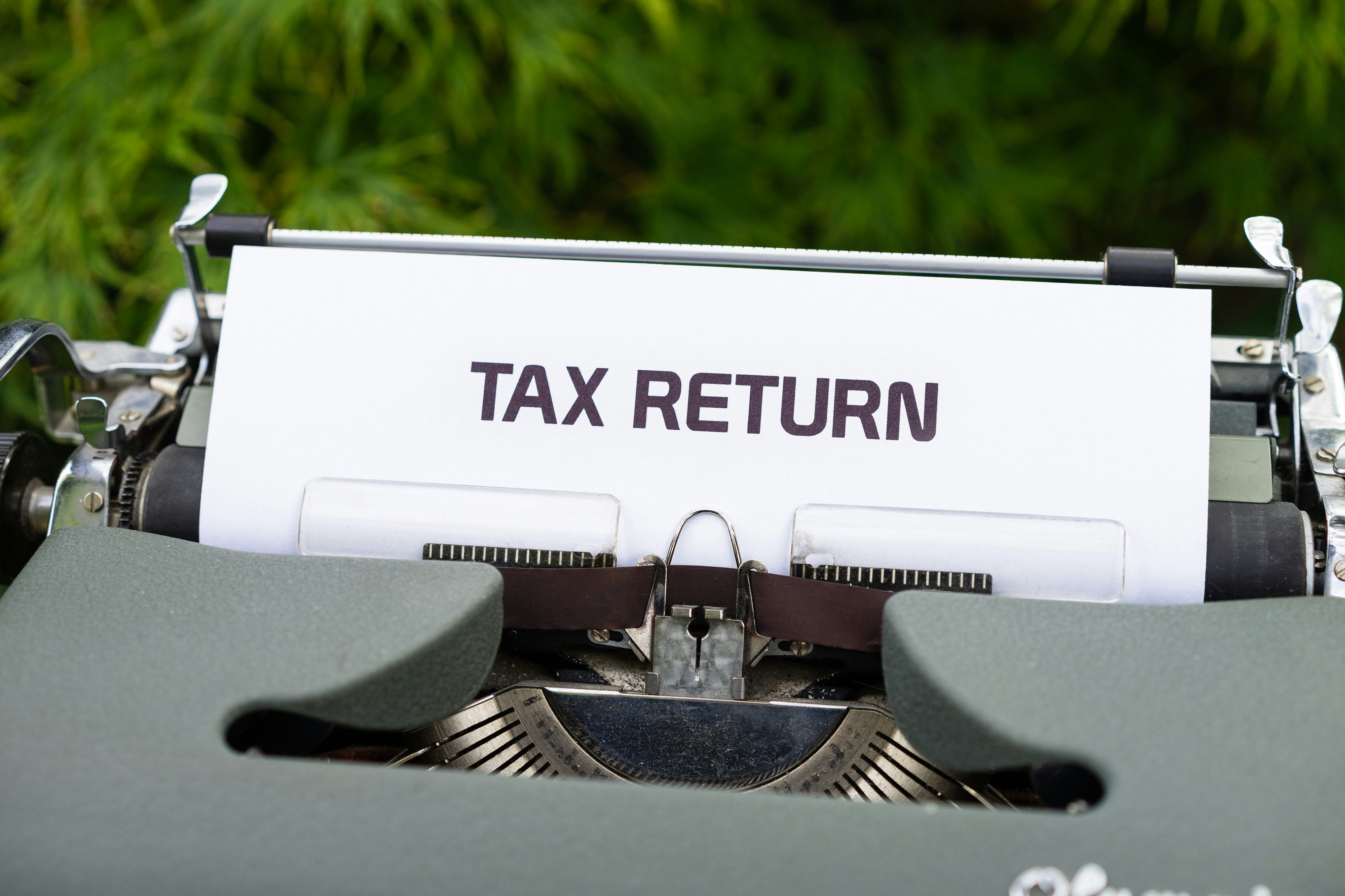 A photograph of an old-fashioned typewriter with the word "TAX RETURN" typed on a white sheet of paper. 