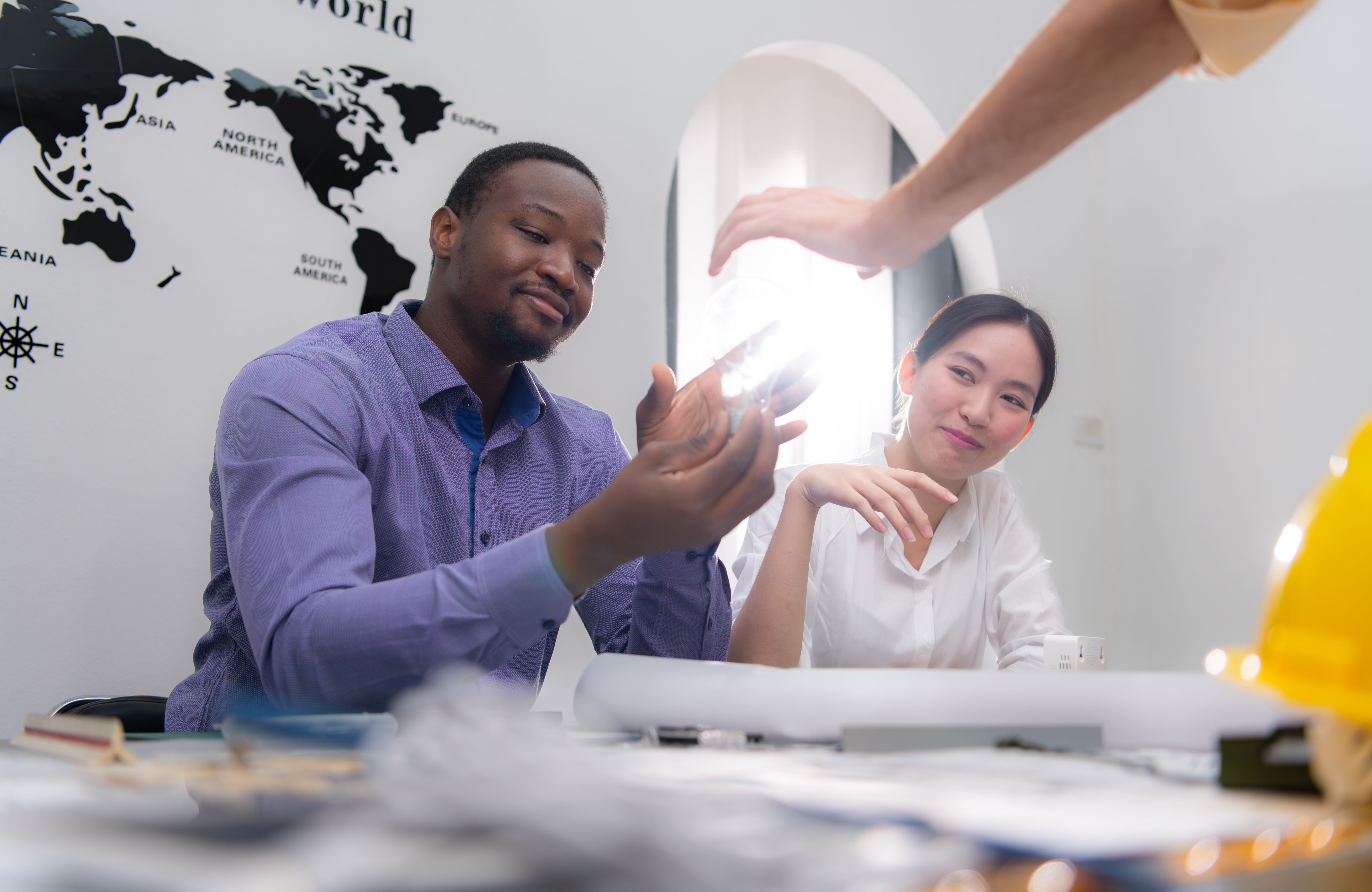 In this photograph, a Black man with a medium build and short hair, dressed in a purple patterned shirt, holds a small, glowing object.