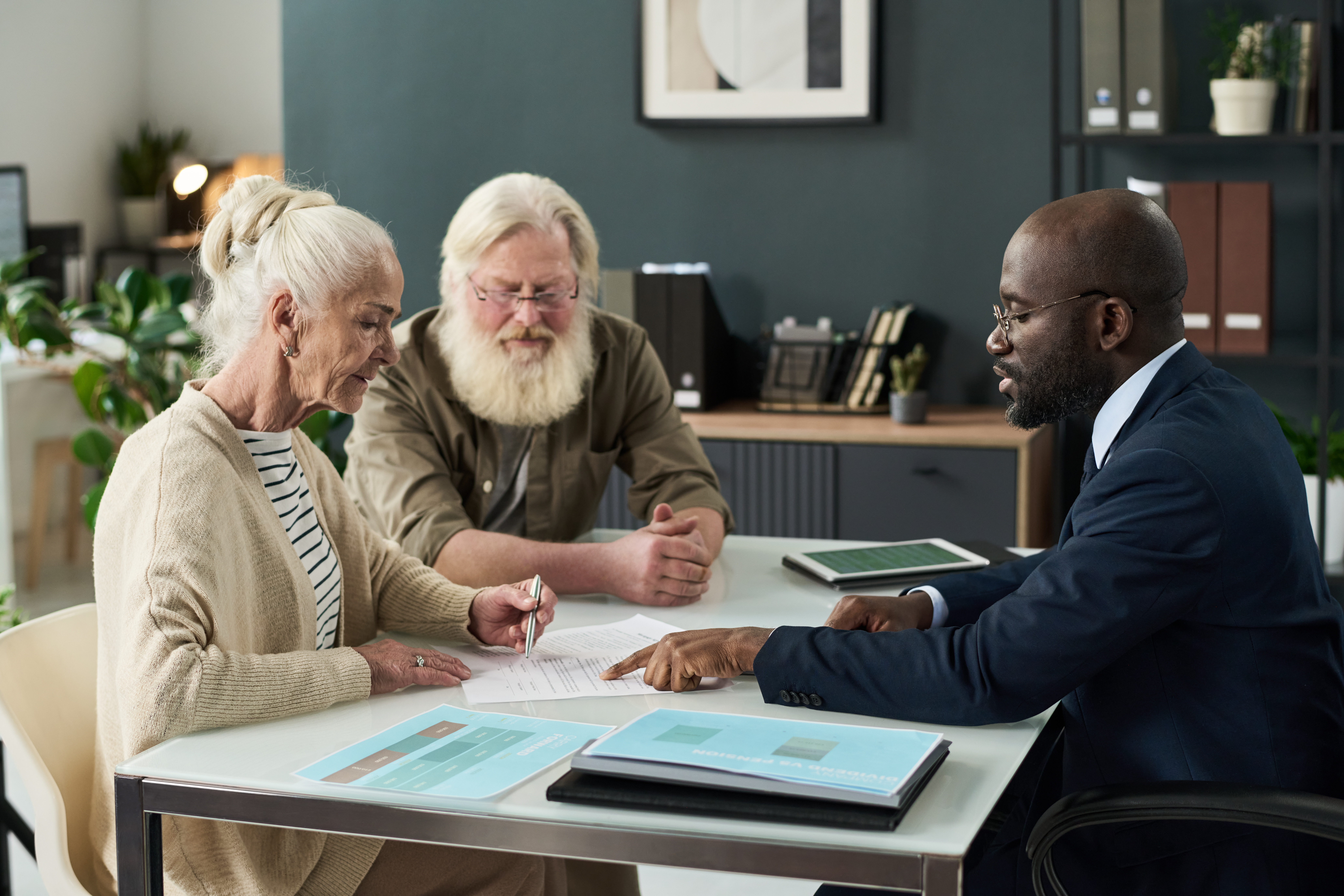 A photograph of three elderly individuals engaged in a business meeting around a white table.