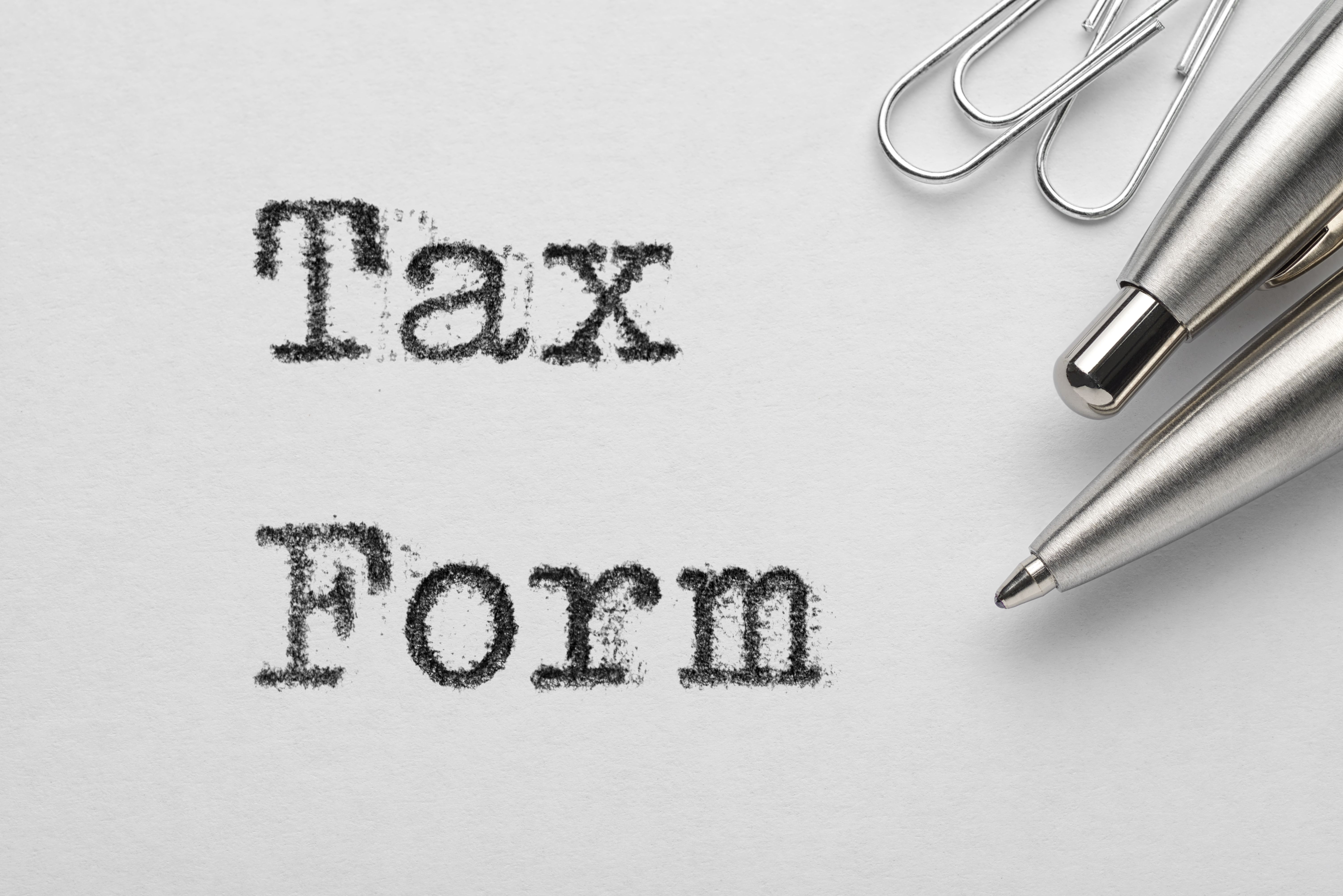 A photograph showcasing a close-up of a white paper with the black, textured word "Tax Form" printed in a bold, serif font.
