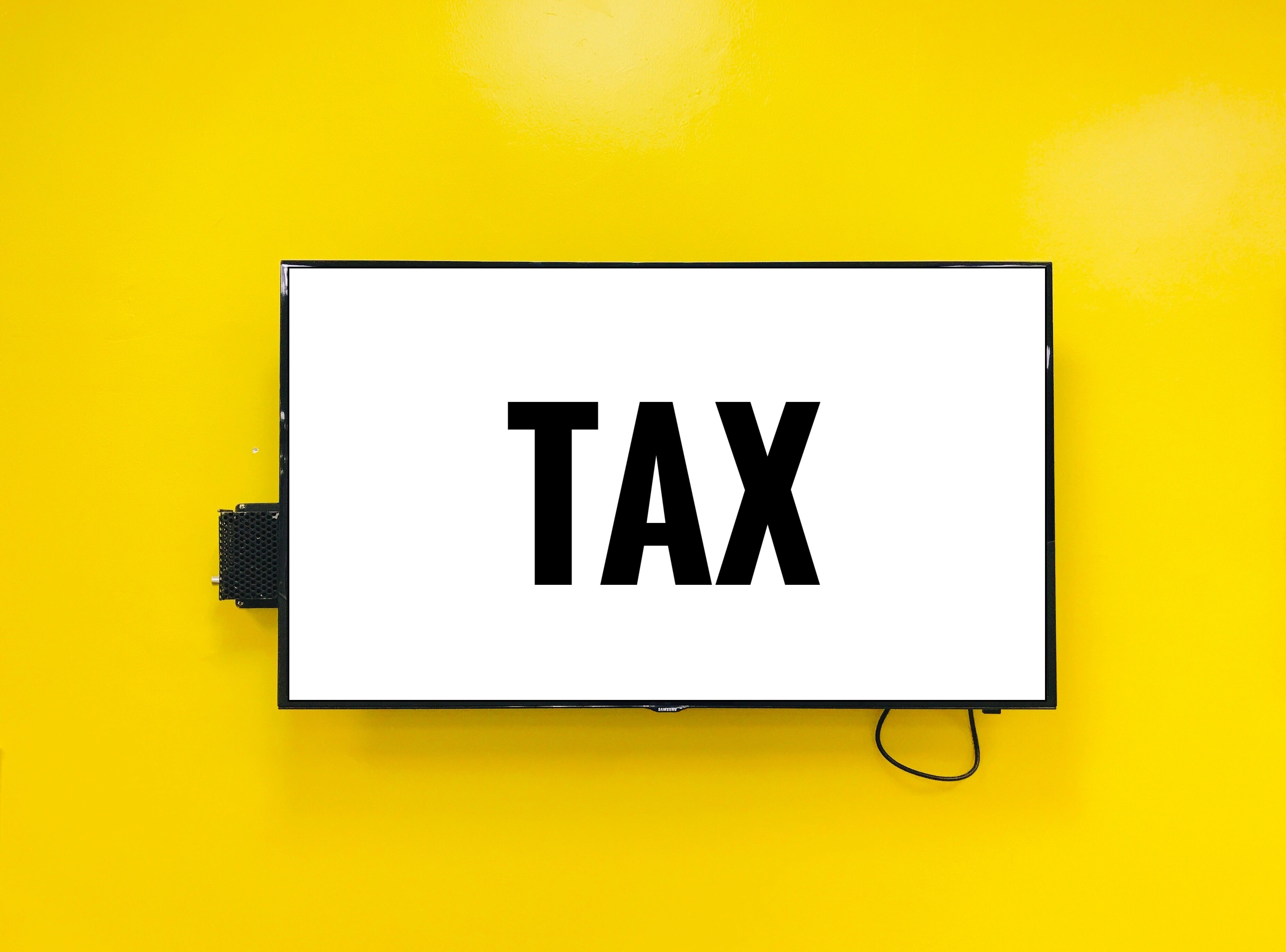 Photograph of a rectangular, black-framed digital display with a bright white background and bold, black text reading "TAX." 
