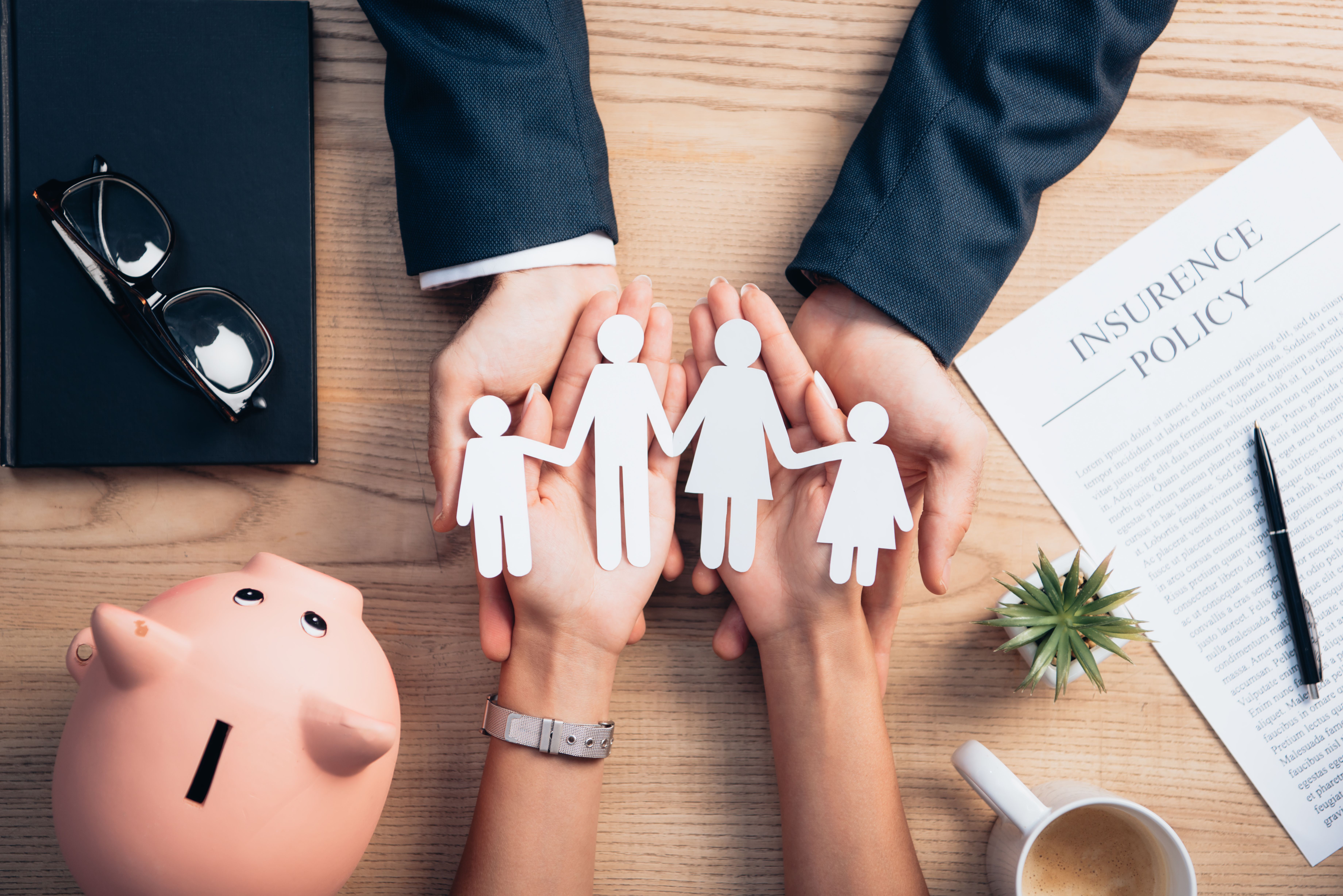 This photograph depicts a wooden desk with a family of five white stick-figure cutouts, representing a couple and their three children. 