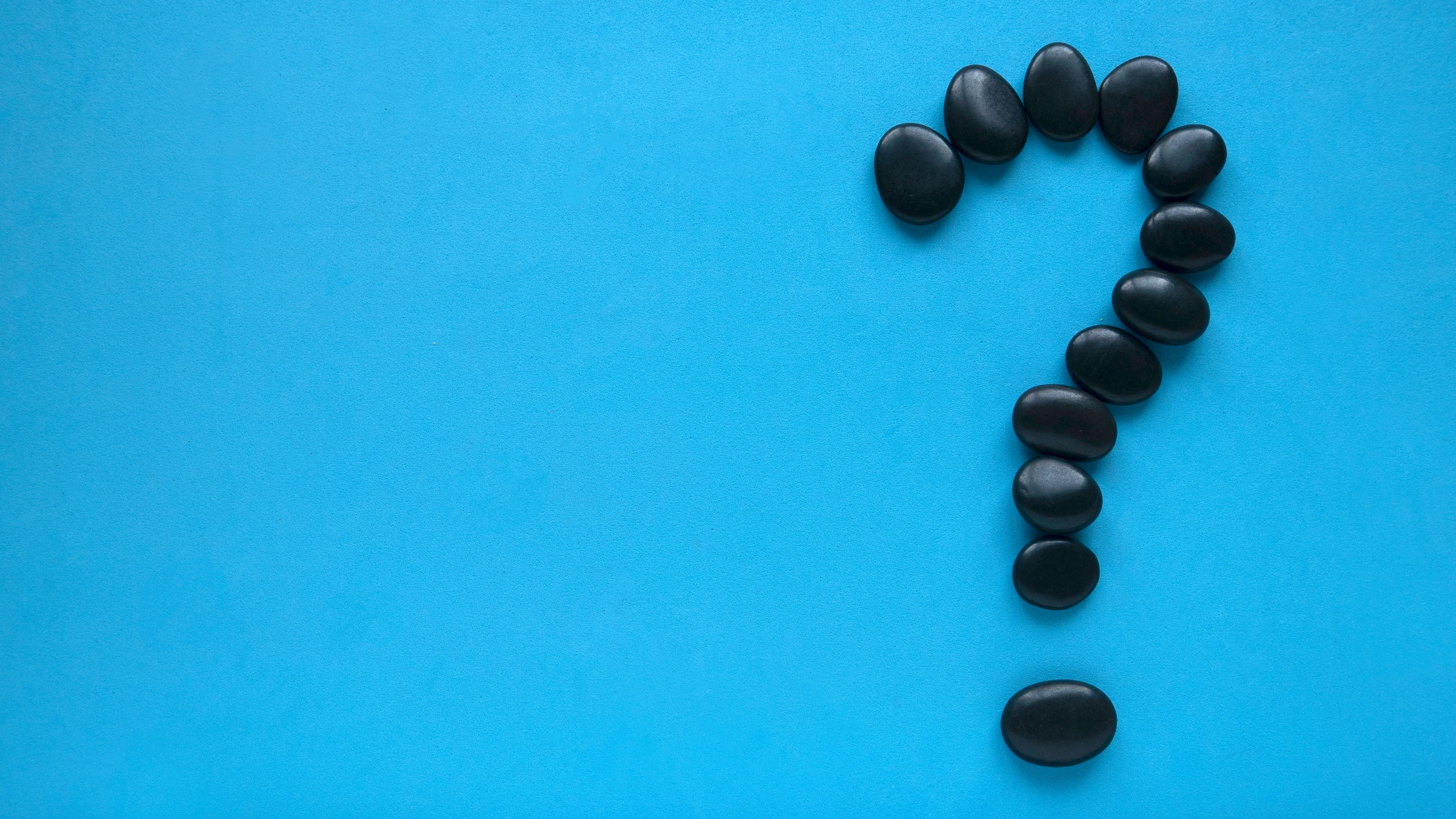 This is a minimalist photograph featuring a single black question mark composed of smooth, round stones