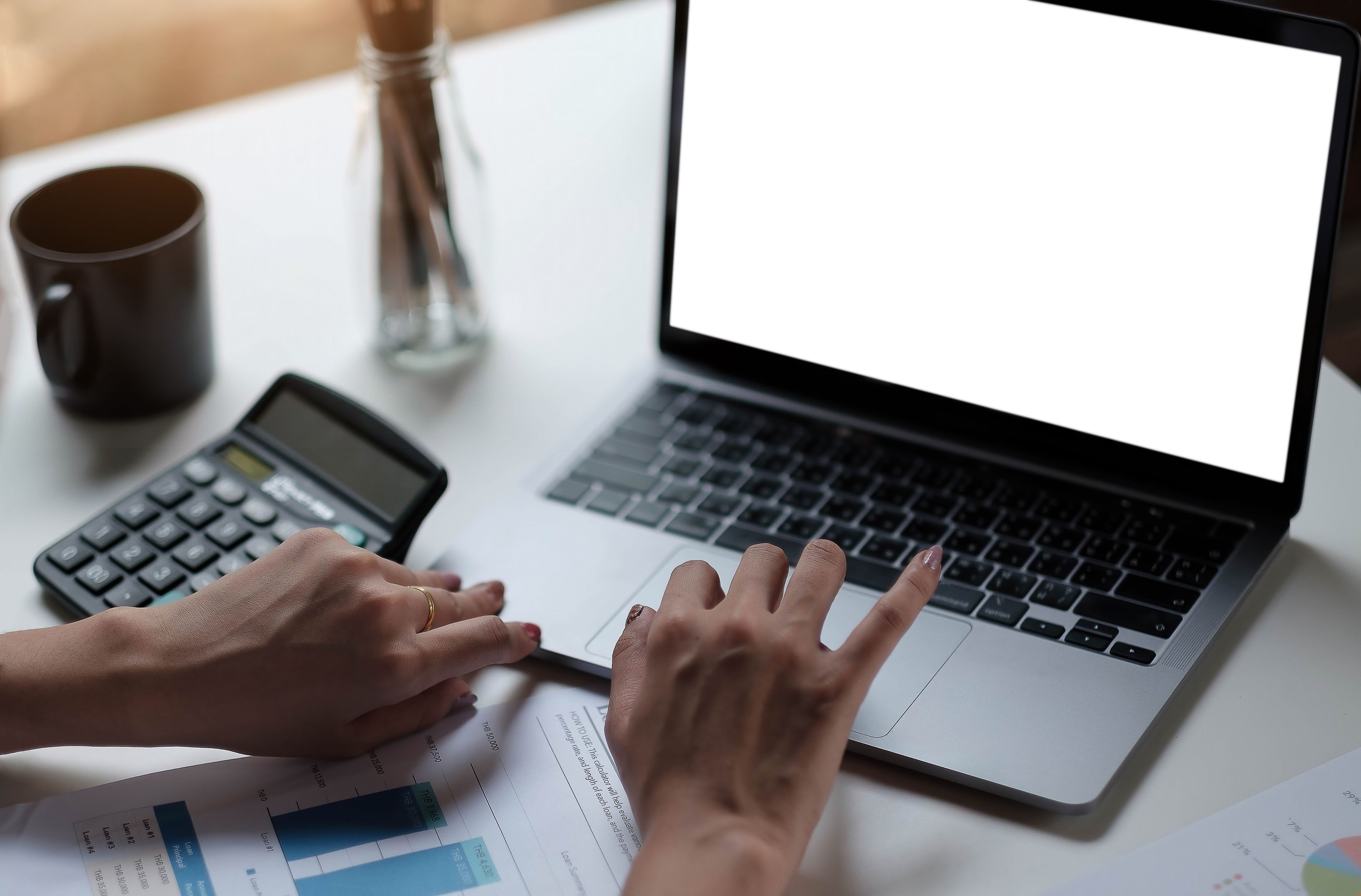 close-up of a person's hands using a silver laptop on a white desk.